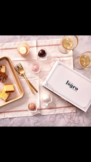 Overhead shot of cake slices, chocolate truffles, champagne glasses, and a bakery box on a striped linen tablecloth.