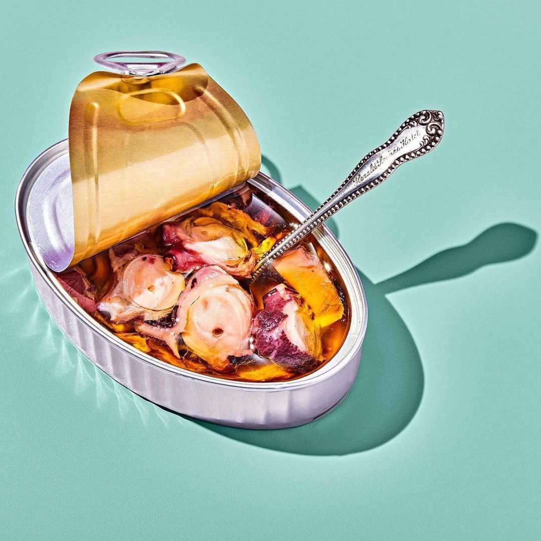 Open silver can of octopus in olive oil, antique spoon inside, teal background, studio lighting, overhead view, gourmet food.