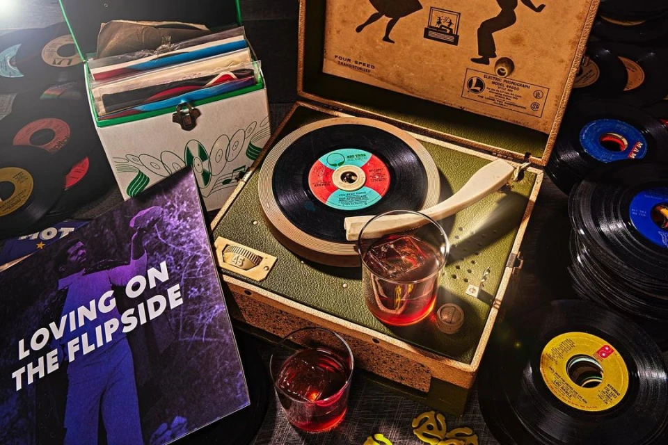 Vintage listening station: A record player spins vinyl beside a glass of liquor and a stack of records, capturing a retro vibe.