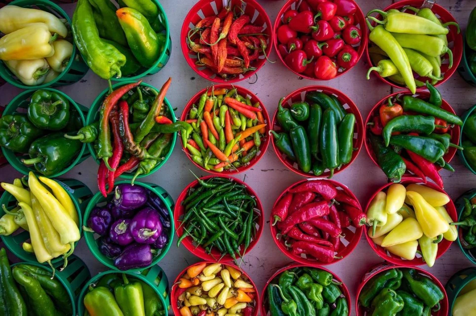 Overhead shot of colorful peppers in round, red and green baskets, arranged on a surface, showcasing variety of colors and shapes.