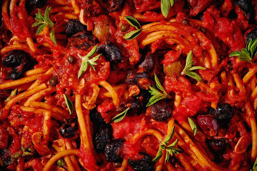 Close-up photo of spaghetti covered in a rich red tomato sauce with olives and fresh basil, creating a visually appealing food composition.