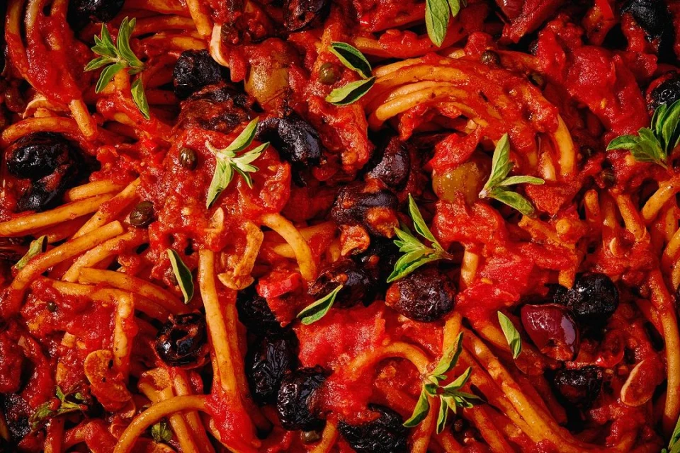 Close-up photo of spaghetti covered in a rich red tomato sauce with olives and fresh basil, creating a visually appealing food composition.