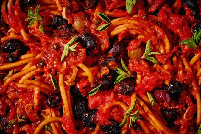 Close-up photo of spaghetti covered in a rich red tomato sauce with olives and fresh basil, creating a visually appealing food composition.