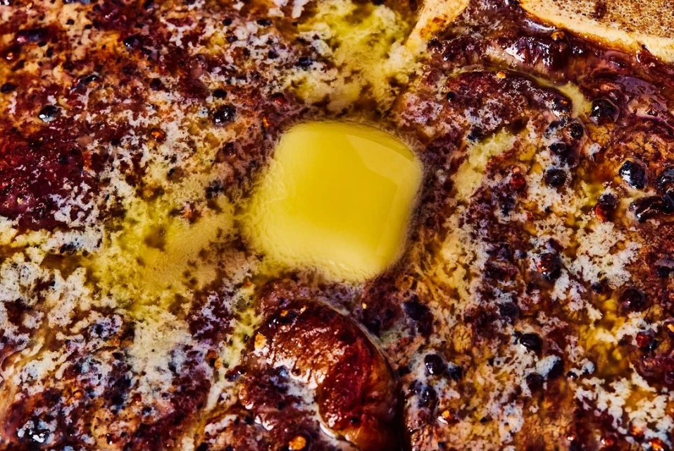 Close-up shot of a steak topped with melting butter, highlighting the textures and colors of the cooked meat and dairy product.