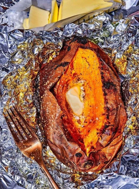 Baked sweet potato served open on foil with butter, accompanied by slices of butter, and a copper-colored fork in the image.