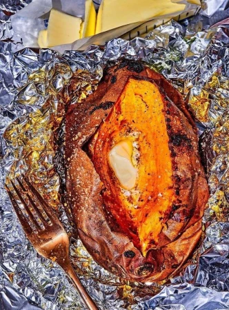 Baked sweet potato served open on foil with butter, accompanied by slices of butter, and a copper-colored fork in the image.