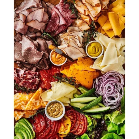 Overhead shot of a wooden charcuterie board filled with assorted meats, cheeses, vegetables, and condiments arranged in sections.