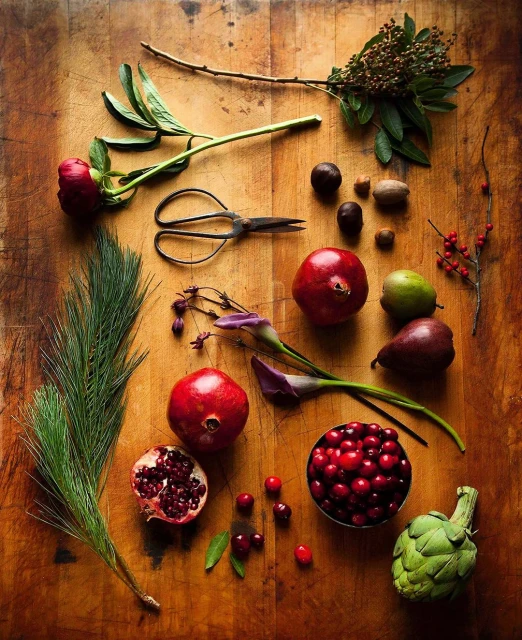Overhead shot on rustic wood table featuring pomegranates, cranberries, pears, artichoke, nuts, flowers, and antique scissors.