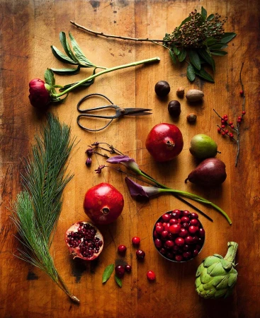 Overhead shot on rustic wood table featuring pomegranates, cranberries, pears, artichoke, nuts, flowers, and antique scissors.