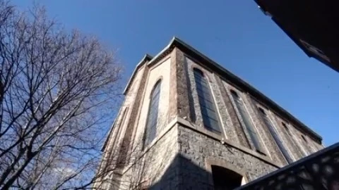 Exterior low-angle view of a tall stone building with arched windows against a clear blue sky, framed by bare tree branches.