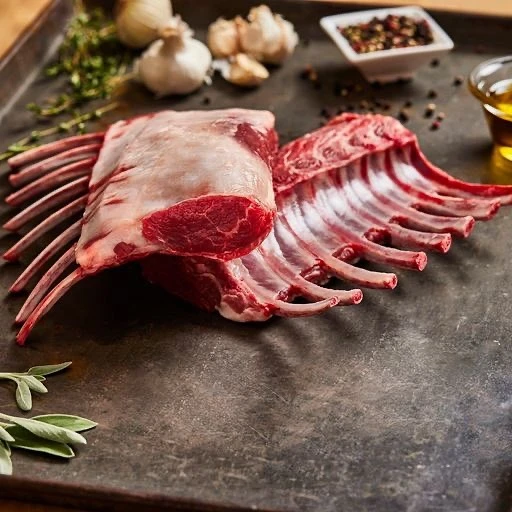 Raw rack of lamb on a dark metal baking sheet with herbs, garlic, peppercorns, and olive oil. Food photography, cooking concept.