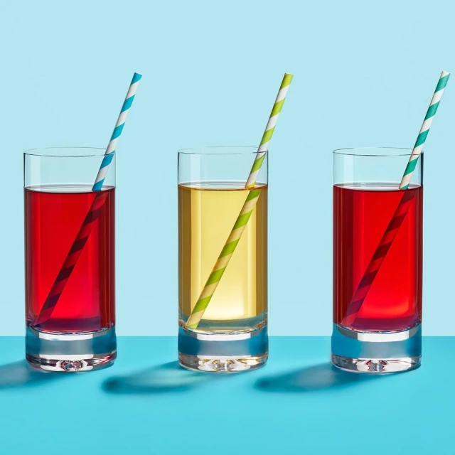 Three refreshing beverages in clear glasses with colorful striped straws, set against a vibrant two-tone turquoise background in studio setting.