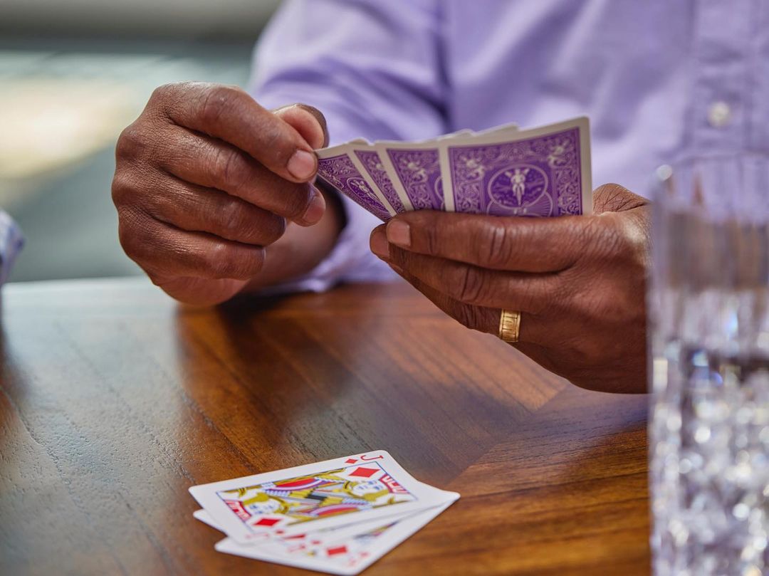 Close-up of a person holding playing cards over a wooden table with a clear glass of water beside the cards.