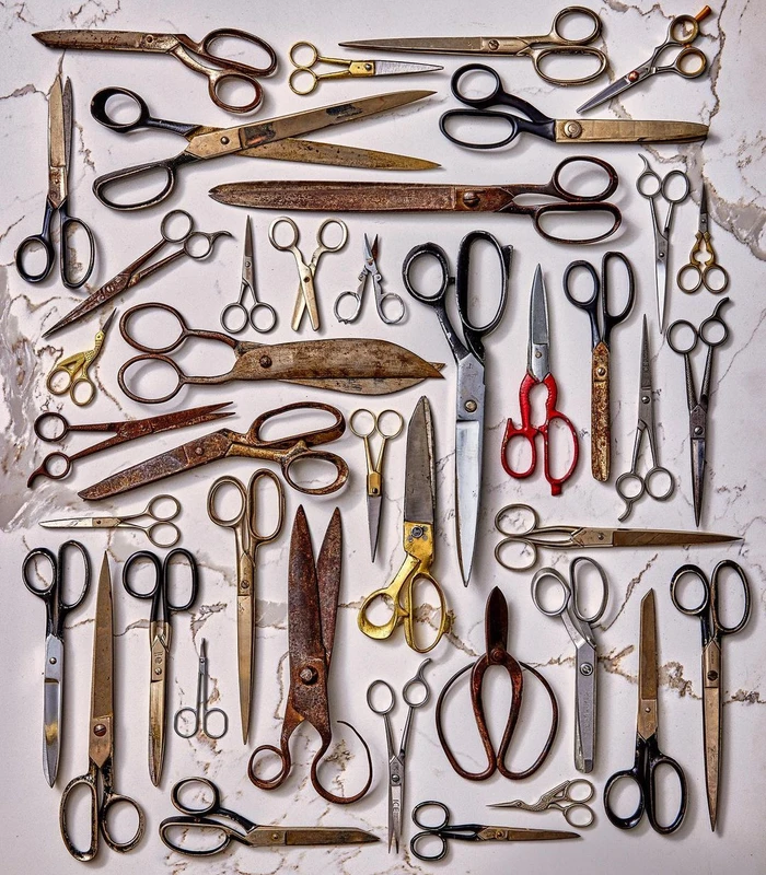 A flat lay of many antique and vintage scissors arranged on a light marble surface.