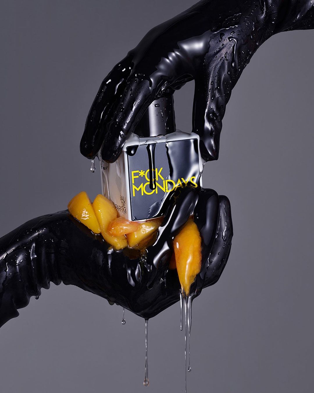 Product shot of a perfume bottle in glossy black gloves, drizzled with dripping liquid and peach slices against a grey backdrop.