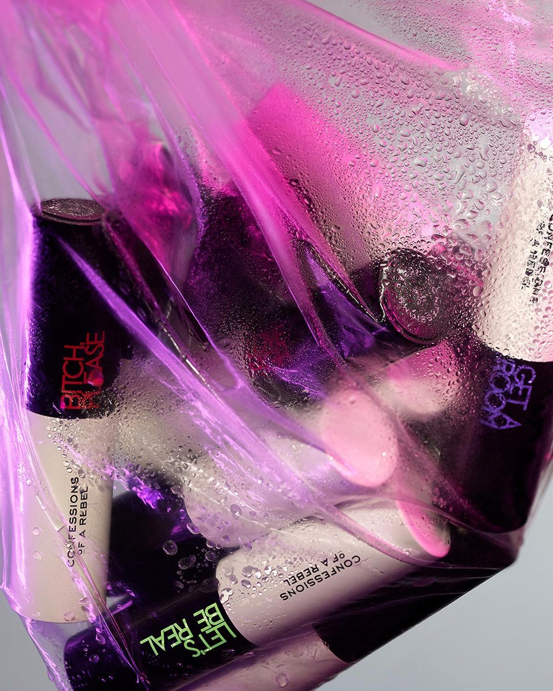 Cosmetic products including lipsticks and compacts in a translucent pink plastic bag with condensation, studio shot.