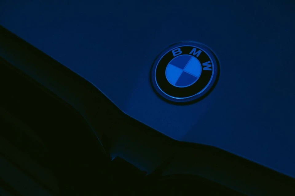 BMW logo on a dark blue car hood, close-up. Automotive branding detail, sleek design, minimal lighting, and shadowed details.