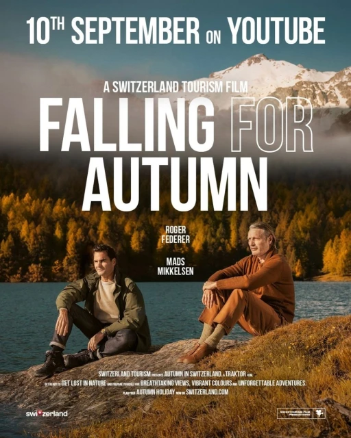 Two men, Roger Federer and Mads Mikkelsen, sit by a lake with autumn trees and a mountain in the background, promoting Switzerland tourism.