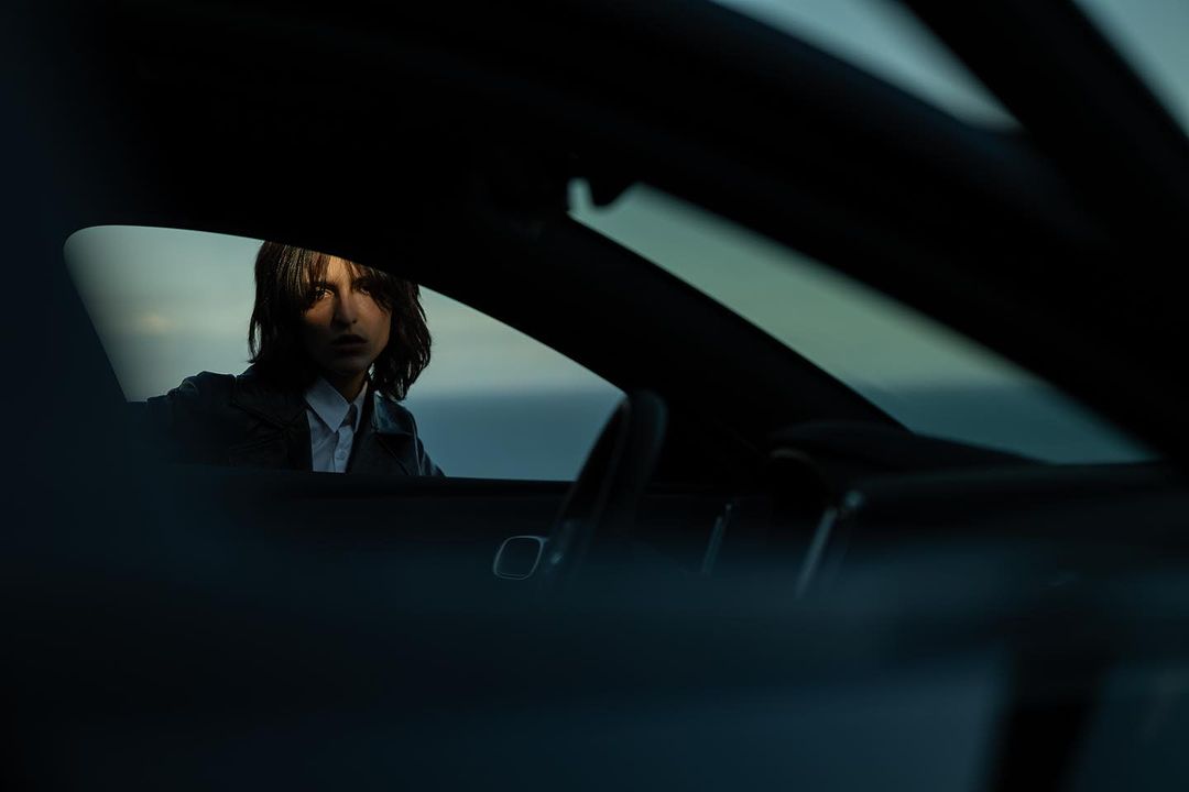 Portrait of a brunette adult woman in a car at dusk, looking out the window toward the ocean horizon. Automotive fashion shot.