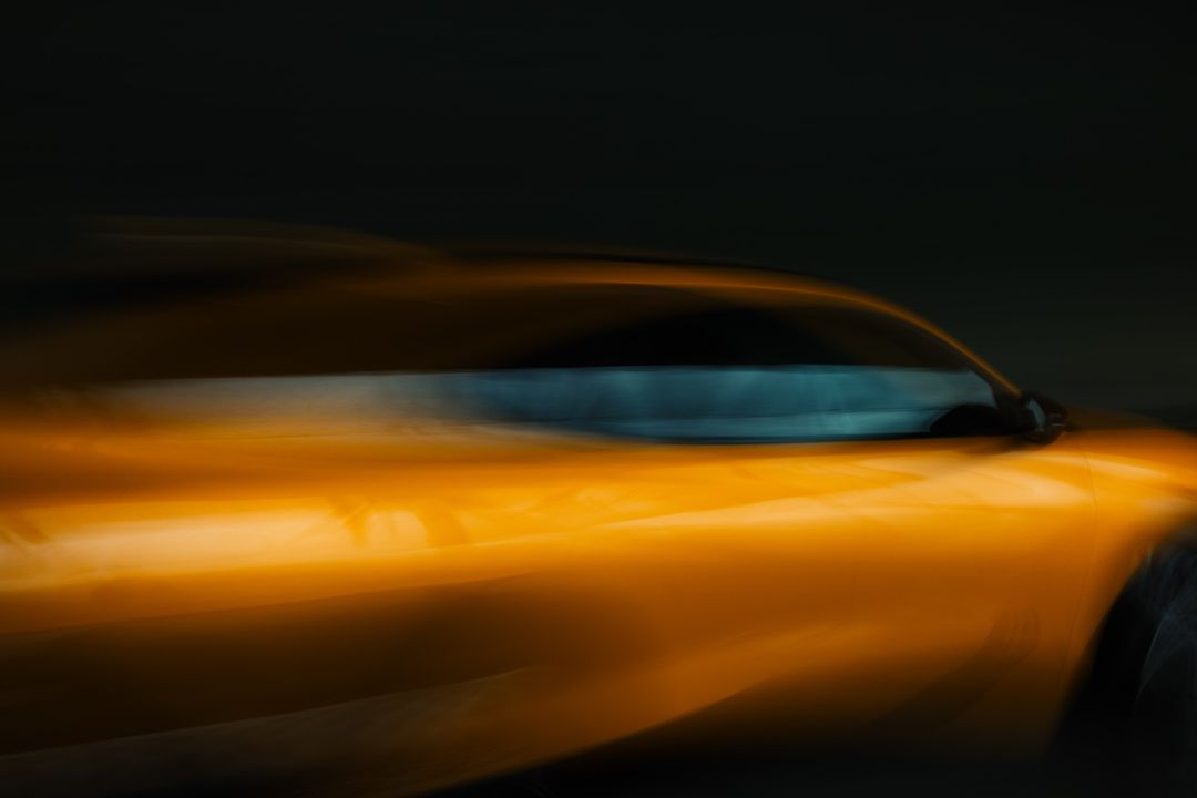 Motion blur image of a yellow car with a sleek design against a dark background. Automotive photography with a sense of speed.