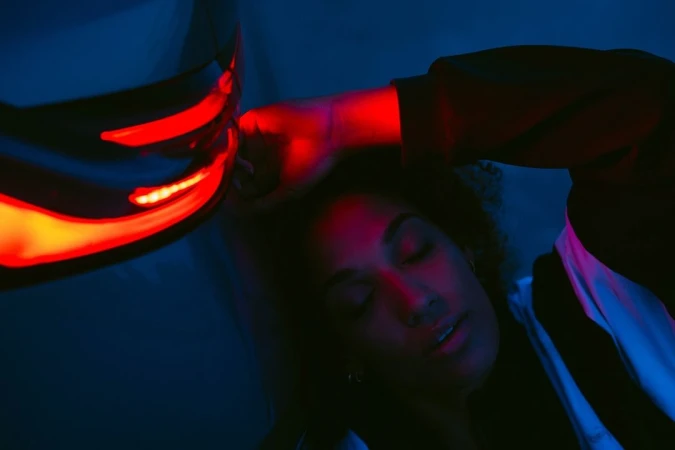 Close-up portrait of a woman with eyes closed next to a glowing red car taillight under blue ambient light