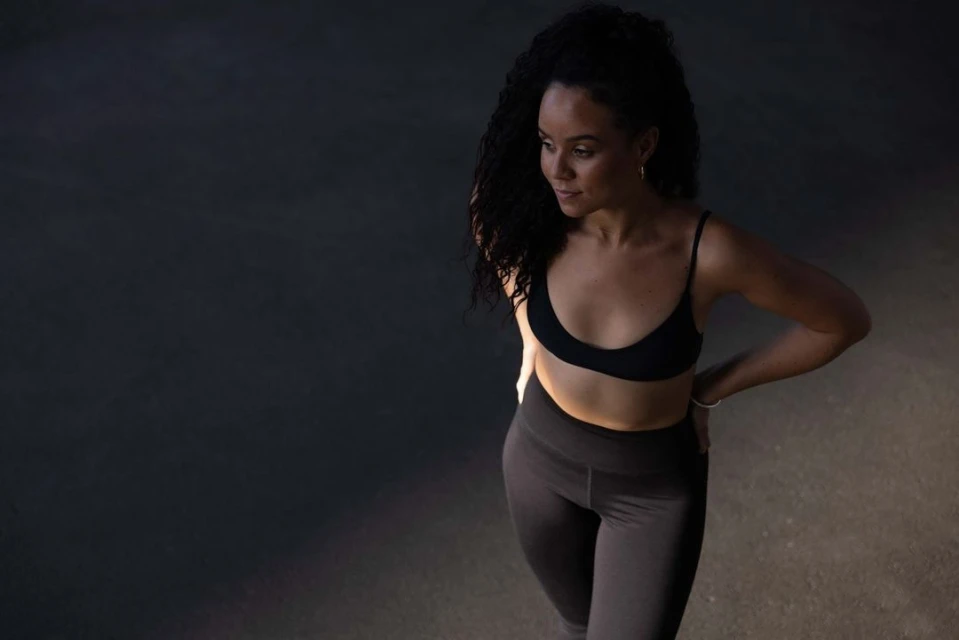 A woman with curly hair is shown in a high-angle shot, wearing a sports bra and leggings against a dark background, creating a modern and sporty visual.
