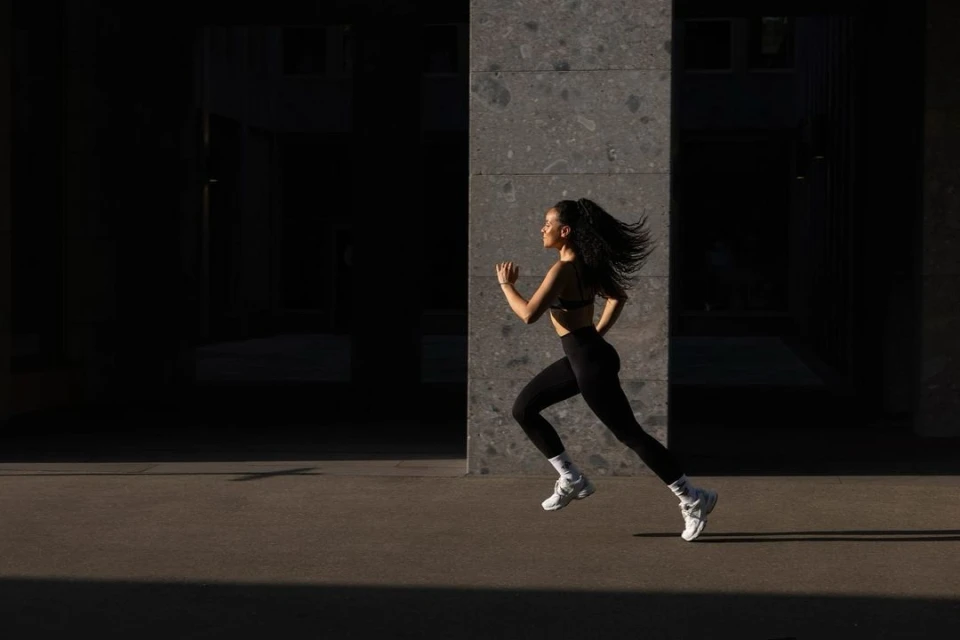 Athletic woman in black activewear running outdoors on a city street on a sunny day. Exercise, fitness, and healthy lifestyle concept.