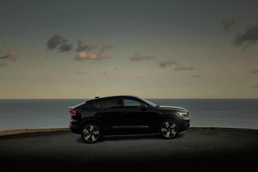 Sleek black Volvo C40 Recharge electric SUV parked against a backdrop of the sea meeting the sky at dusk.