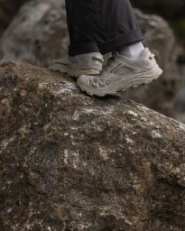 Close-up shot of hiking shoes on a person stepping over large textured rocks in a natural outdoor environment.