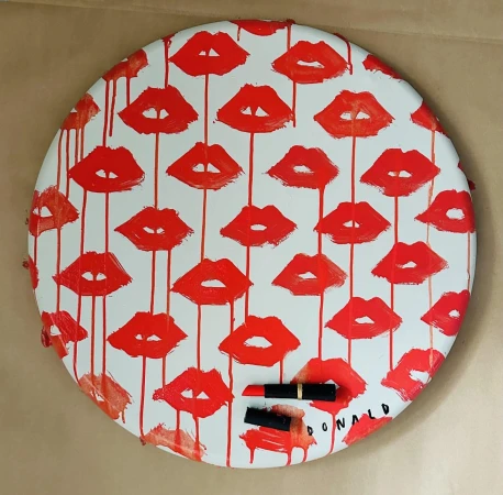 A round white canvas featuring a repeating pattern of red lips with red paint drips, with two lipsticks at the bottom.