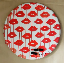 A round white canvas featuring a repeating pattern of red lips with red paint drips, with two lipsticks at the bottom.