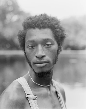 Black man with short afro and chin beard wearing overalls and silver chain necklace in portrait by Donavon Smallwood