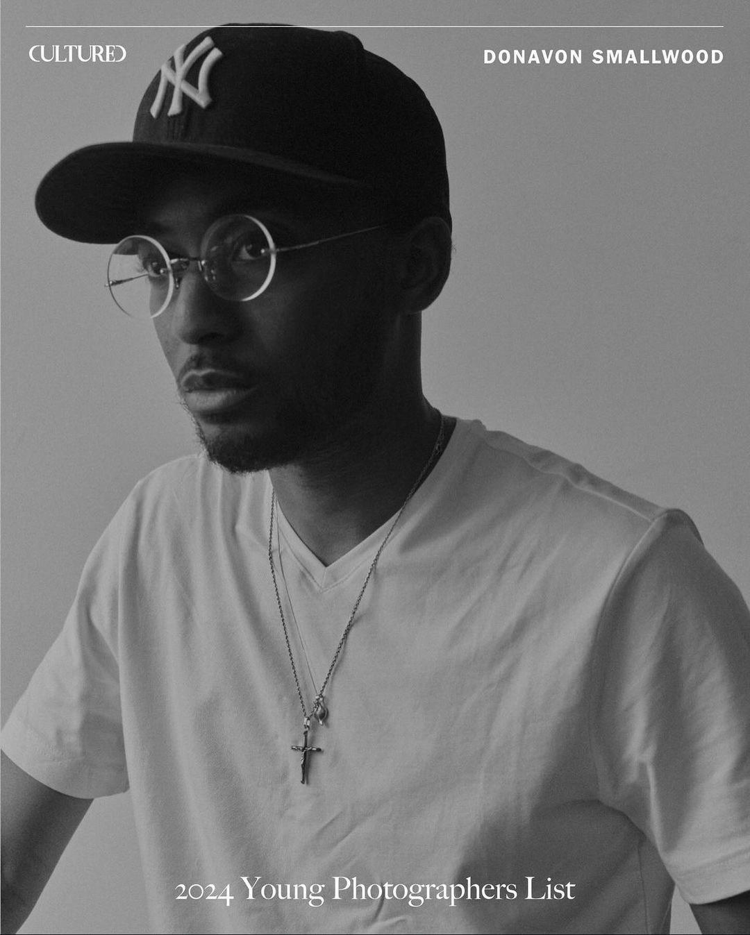 Black and white portrait of Donavon Smallwood wearing a New York Yankees baseball cap and round glasses, with a white t-shirt.