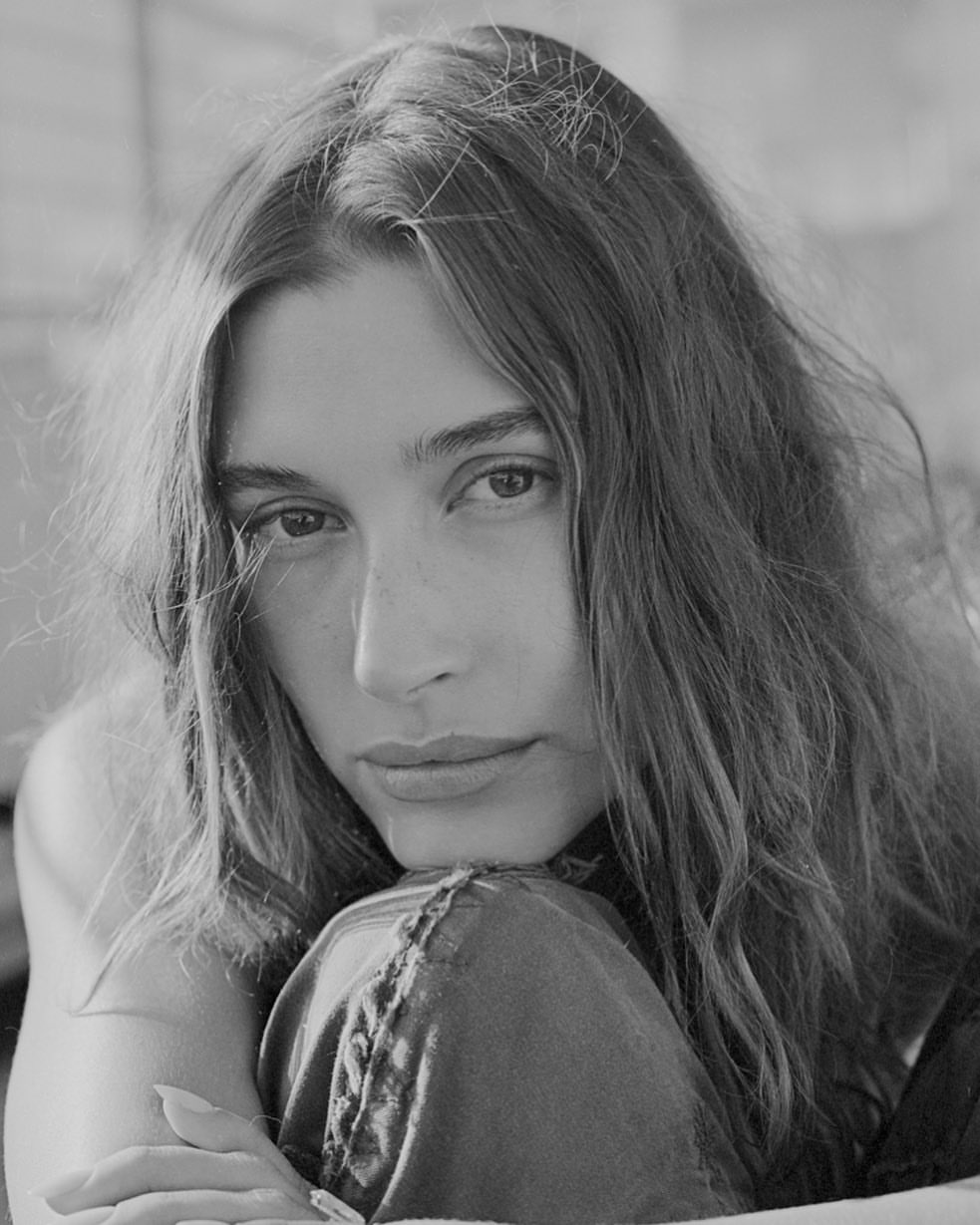Black and white close-up of a fair-skinned adult woman with long brown hair, wearing casual clothes and resting her head on her arm.