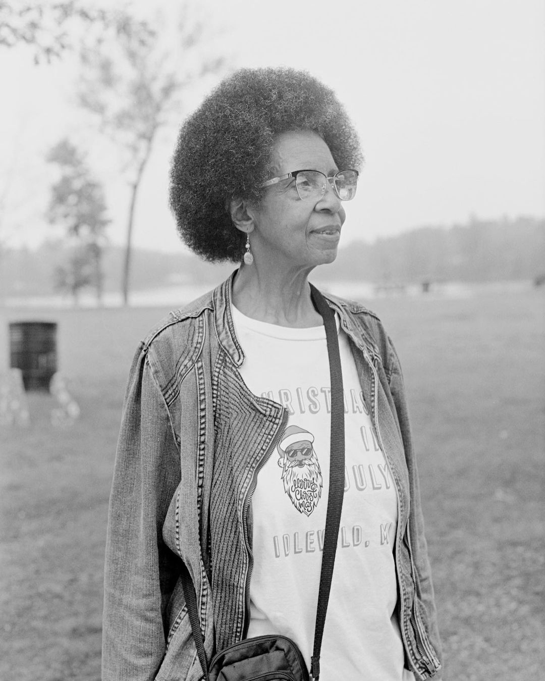 Monochrome portrait of an elderly Black woman wearing glasses, a patterned t-shirt, and a jacket outdoors in New York.