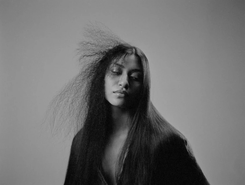 Striking black and white portrait of a woman with dramatic hair, looking down in a studio setting.  Fashion and beauty photography.