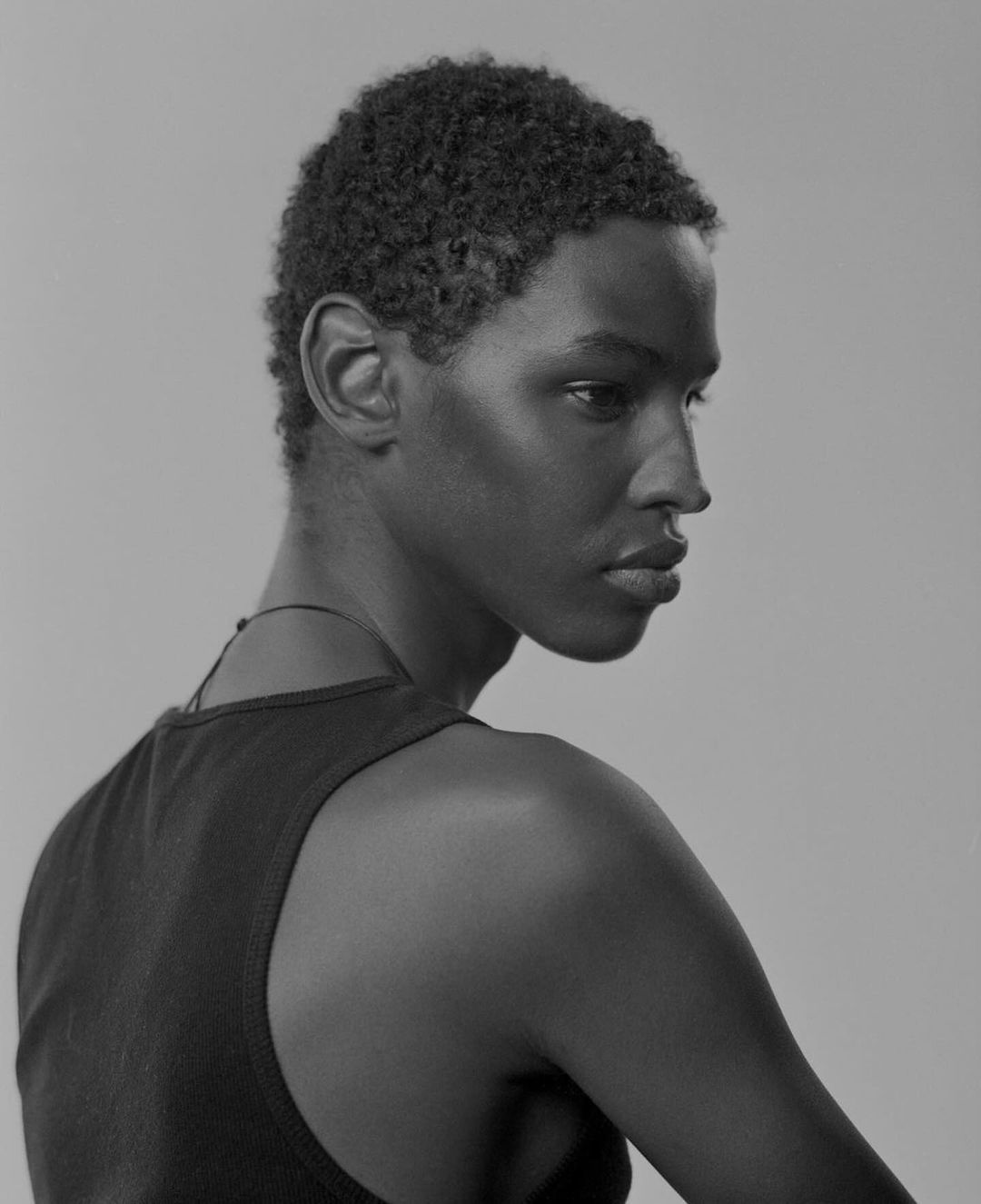 Striking black and white portrait of a young African-descent adult male looking off-camera, with a neutral expression in a neutral environment.