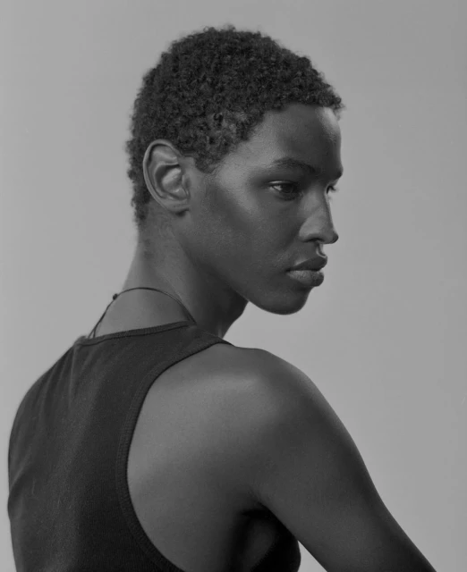 Striking black and white portrait of a young African-descent adult male looking off-camera, with a neutral expression in a neutral environment.