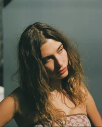 Portrait of a woman with long wavy brown hair wearing a patterned strapless top under direct sunlight