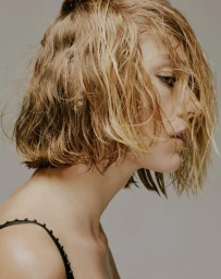 Profile portrait of a woman with wet blonde hair wearing a black strap top against a plain grey background