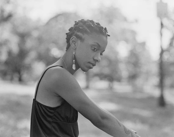 Black woman with braided hair and drop earrings in a dark strap top outdoors, photographed by Donavon Smallwood.