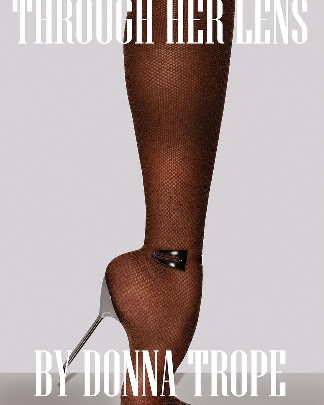 A woman's leg clad in textured hosiery and a high-heeled shoe with metal accents, set against a neutral backdrop and bright lighting.
