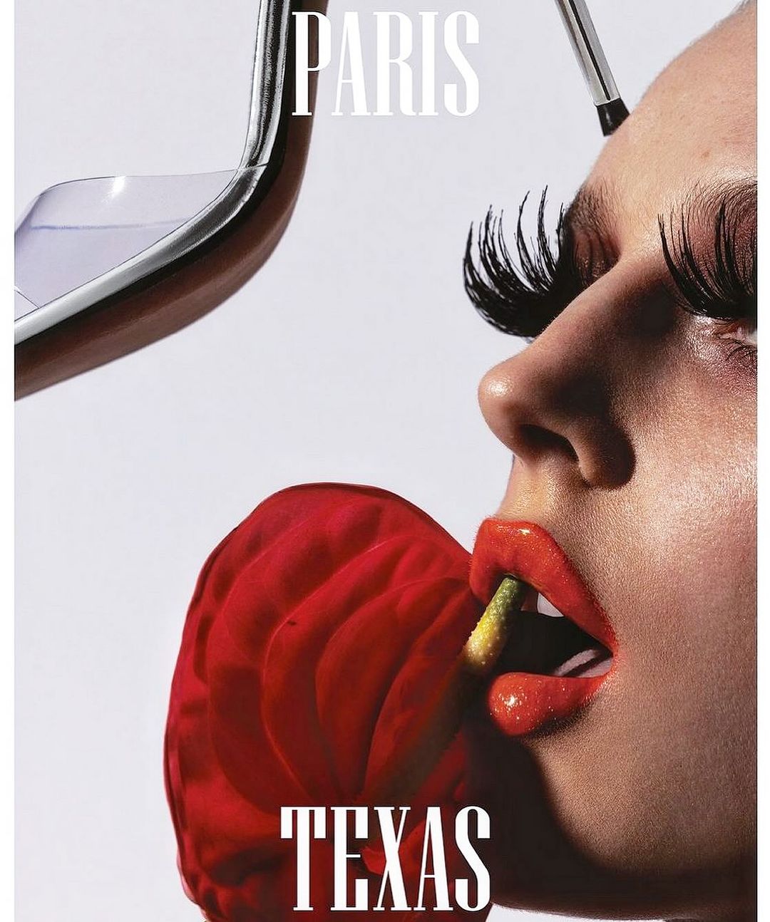 Close-up of a woman's face with red flower in her mouth, dramatic lashes, makeup brush near forehead, and white PARIS/TEXAS text overlay.