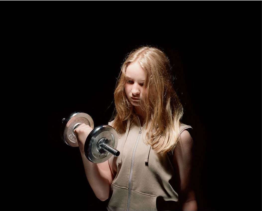 Young woman lifts dumbbell in a fitness workout with a dark background. Athletic training and strength exercise in a studio setting.