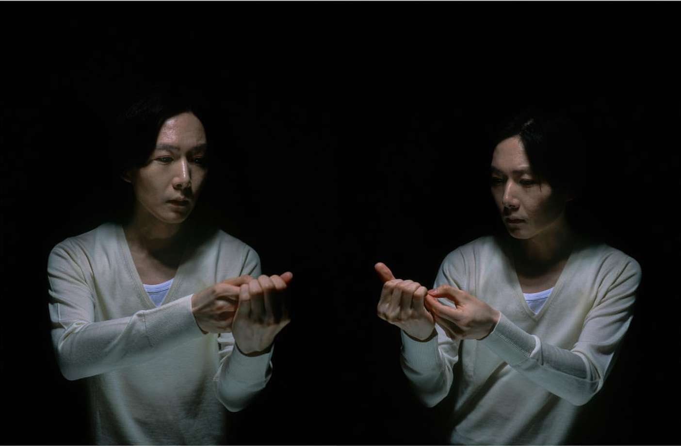 A split-screen effect with two Asian adults dressed in light sweaters, each holding their hands in front in an indoor setting with dark lighting.