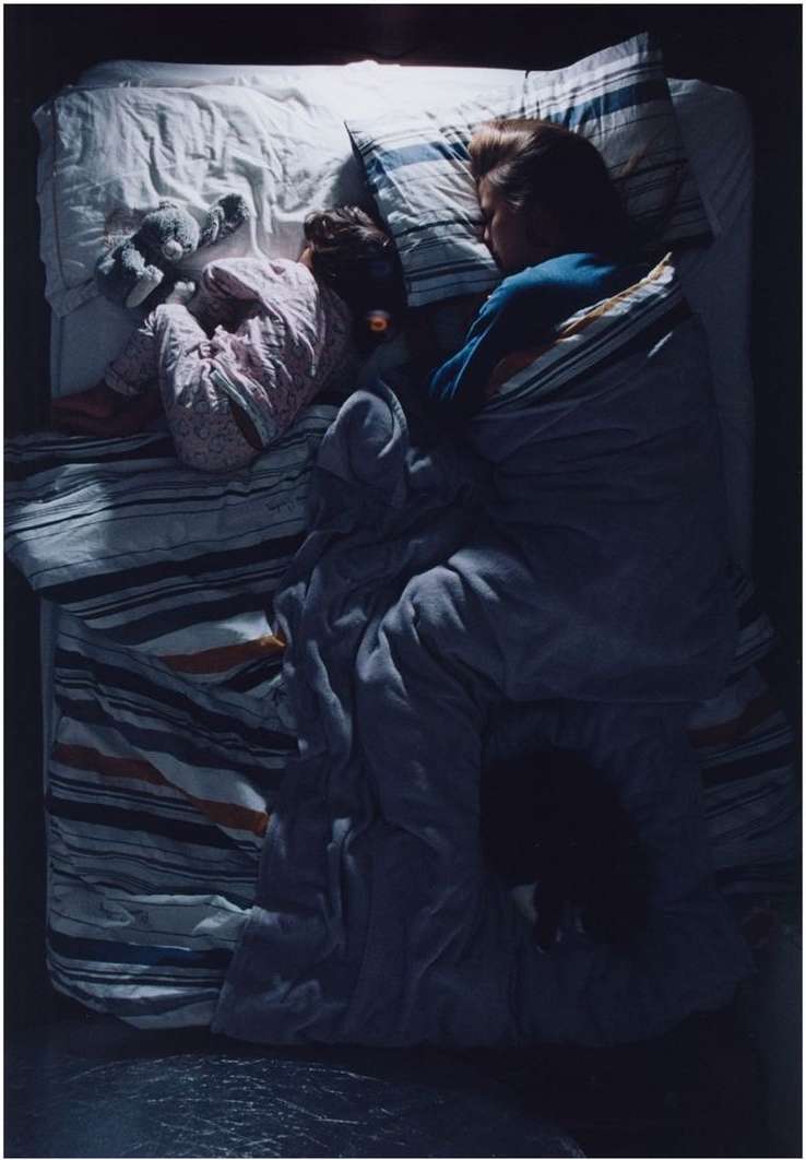 Overhead shot of two children sleeping in a bed with striped bedding, with a soft toy beside one of them in the dimly lit room.