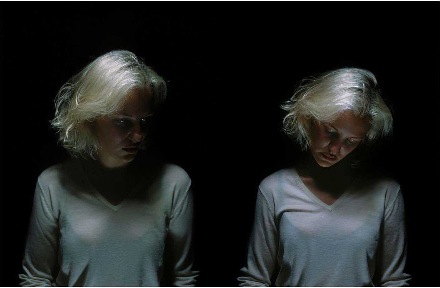 Two blonde women wearing white V-neck tops posed against a pitch black background in low key lighting by photographer Dorothy Sing Zhang
