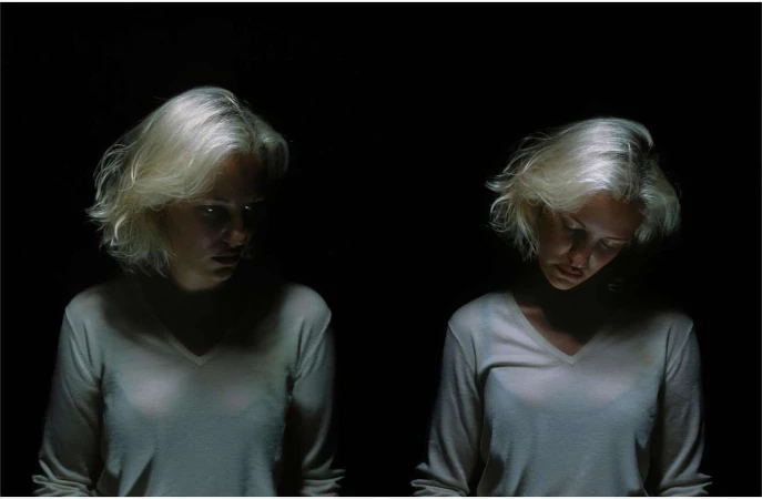 Two blonde women wearing white V-neck tops posed against a pitch black background in low key lighting by photographer Dorothy Sing Zhang