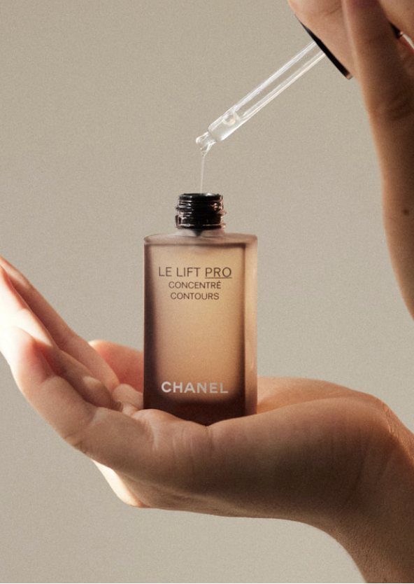 Cosmetic serum bottle with dropper held over woman's hand, neutral studio background, skincare product shot, Le Lift Pro Concentre Contours.