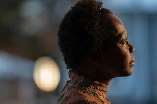 Profile of a black woman with an updo, wearing a patterned top against a blurred background, creating a soft, contemplative portrait.
